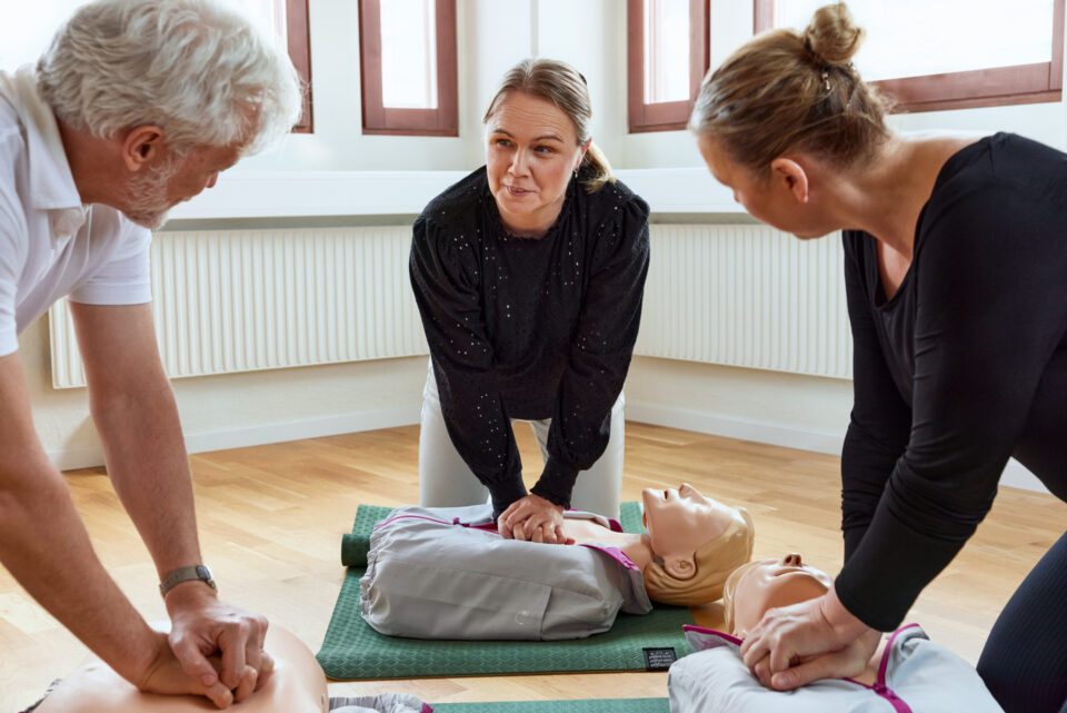 Sjuksköterska instruerar två personer i HLR